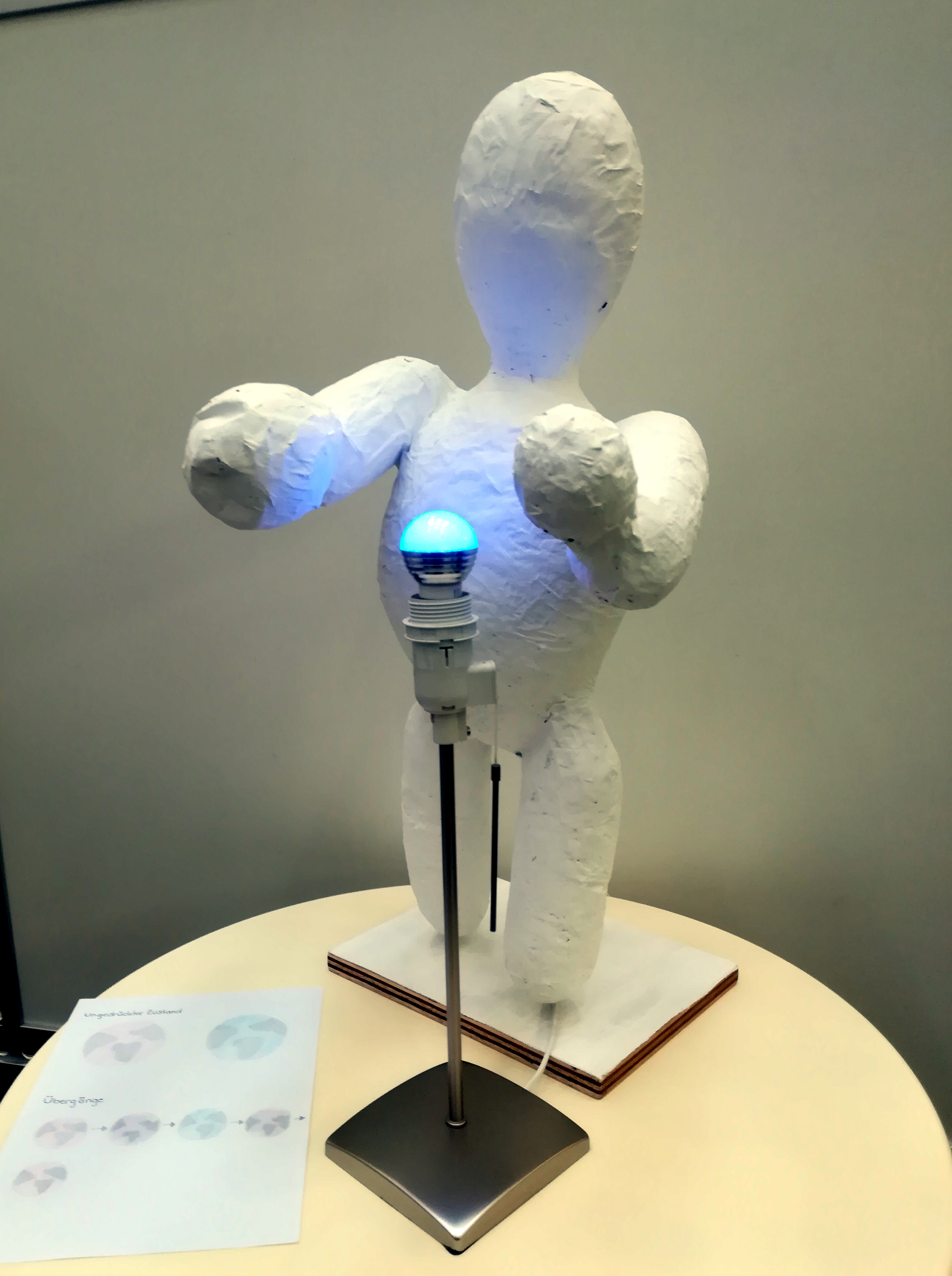 Eine weiße Figur aus Pappmasché, in den Händen eine kleine Kugel, die nun blau leuchtet